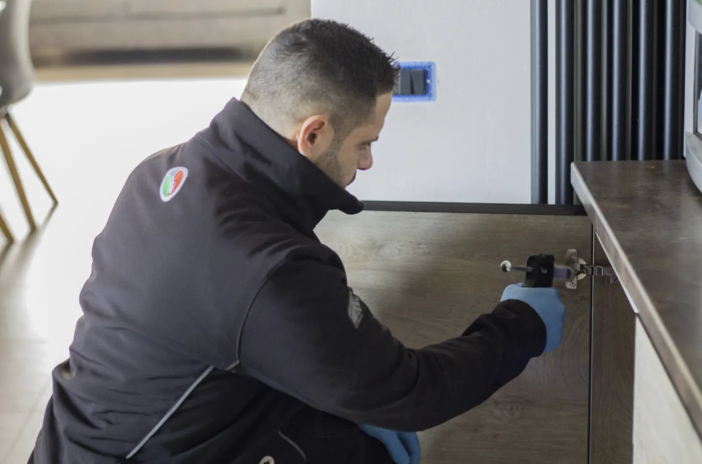 Tecnico Ital Disinfestazioni applica trattamento mirato in cucina con guanti e attrezzatura professionale